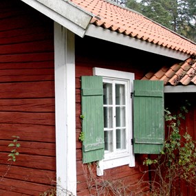 Detalj av falurött torp med spröjsat fönster och gröna fönsterluckor