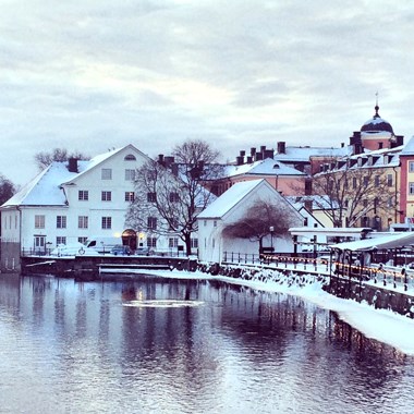 en vinterbild på en vit, äldre stenbyggnad vid en å i stadsmiljö.