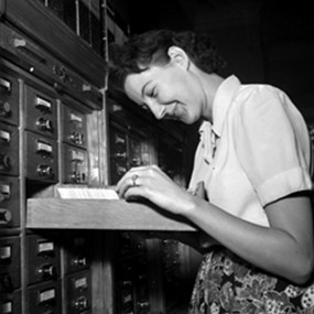 Kvinna står och bläddrar bland kort som ligger i ett arkivskåp.