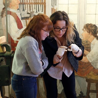 En museipedagog och en besökare tittar nära på en silversked från 1700-talet.
