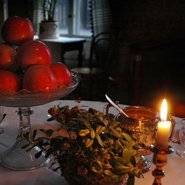 Röda äpplen i en skål och ett tänt stearinljus på ett bord.