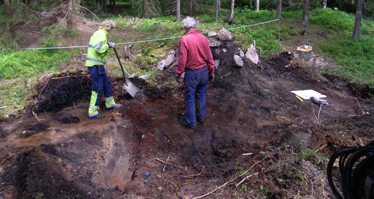 En man och en kvinna undersöker lämningarna efter en kolarkoja i skogen.